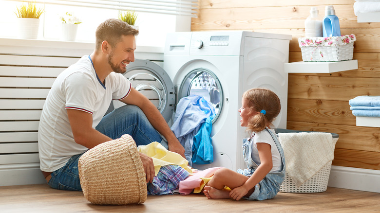 A father and a young girl sitting by a washing machine