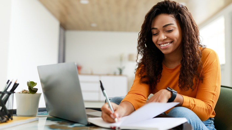 Woman takes notes while using laptop 