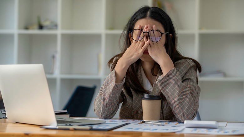 Stressed woman rubs eyes at work desk