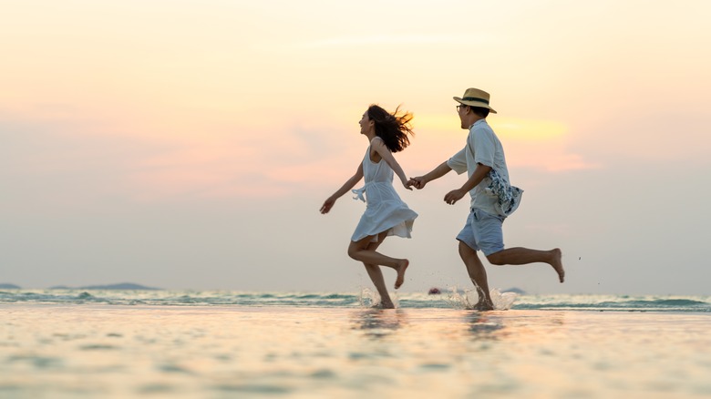 couple holding hands running at beach