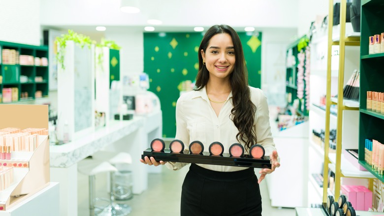 Beauty store employee holds display of blush shades 