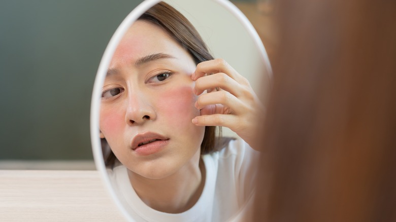 Woman examining red, irritated skin in mirror