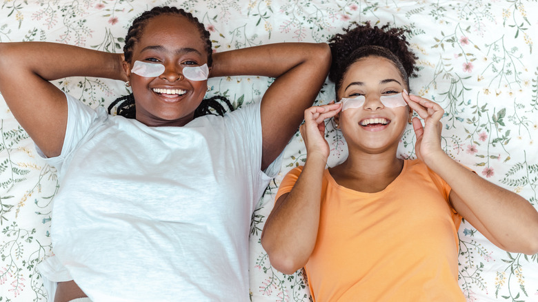 Two women on bed wearing skincare treatment pads 