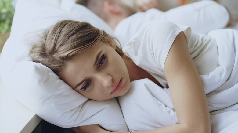 Sad woman in bed with back to partner