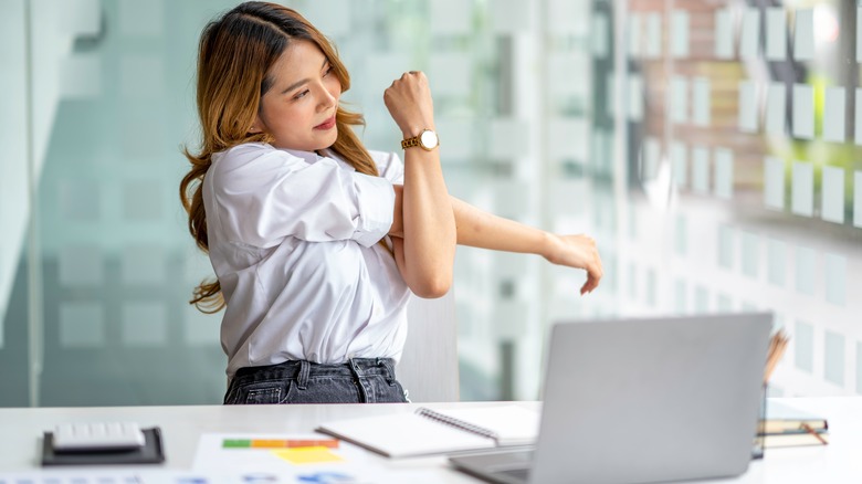 Woman stretching at desk in front of computer