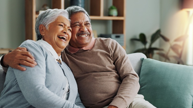 An older couple cuddling and smiling on the couch.