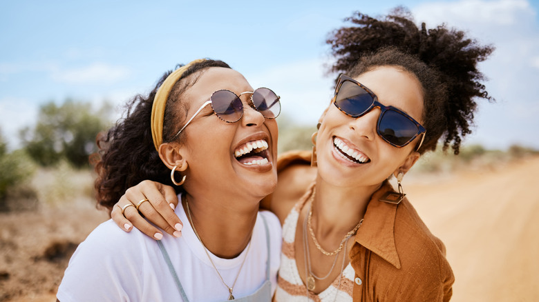 Two women in sunglasses laughing together in a rural area.