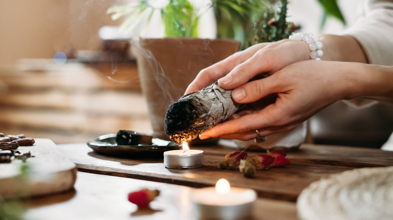 Closeup of a woman lighting a smudge stick with a candle 