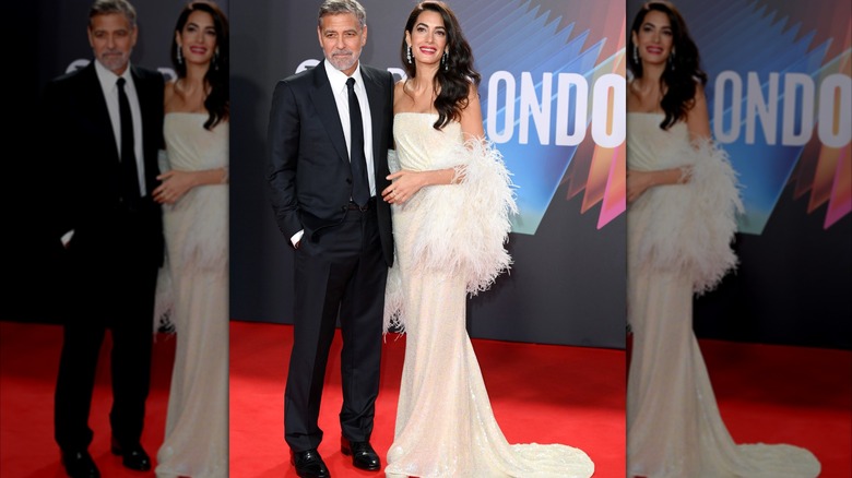 Amal Clooney with feather boa, posing in a white dress next to George Clooney on the red carpet