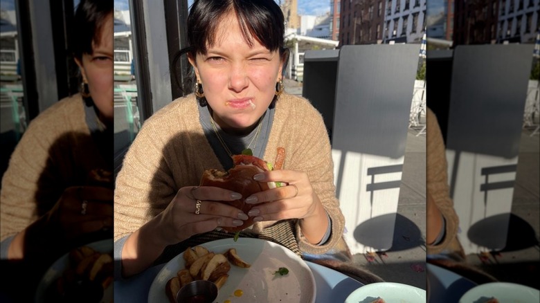 Millie Bobby Brown eating a burger in a cozy outfit.