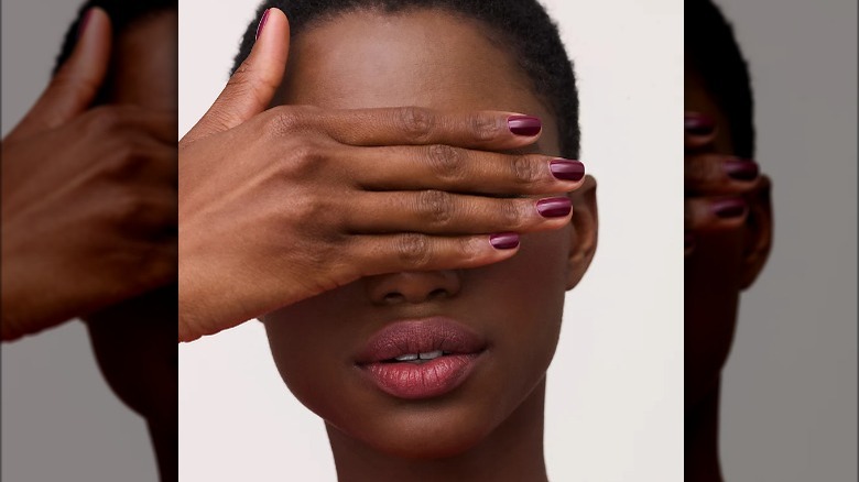 woman covering eyes with plum nails