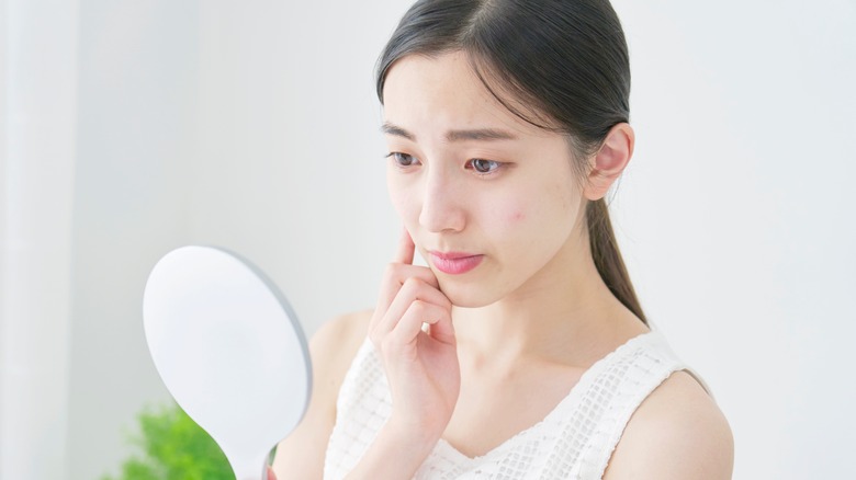 woman looking at pimple in mirror