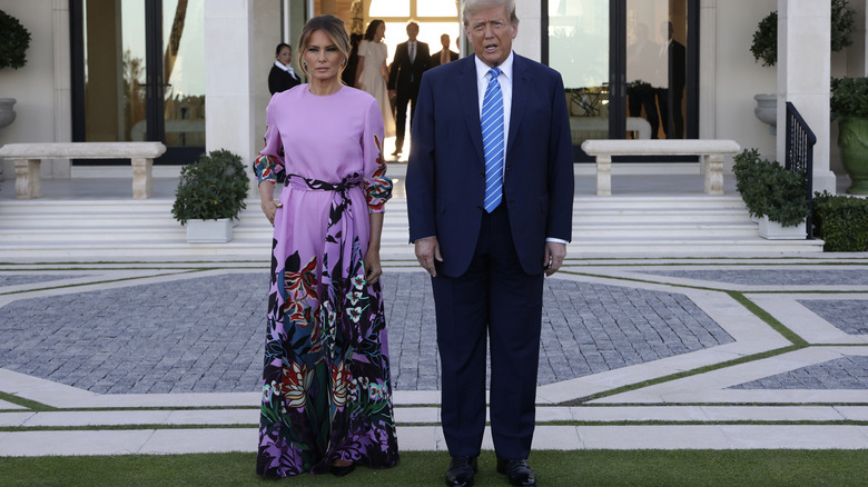 Melania Trump with Donald Trump, wearing a purple floral jumpsuit