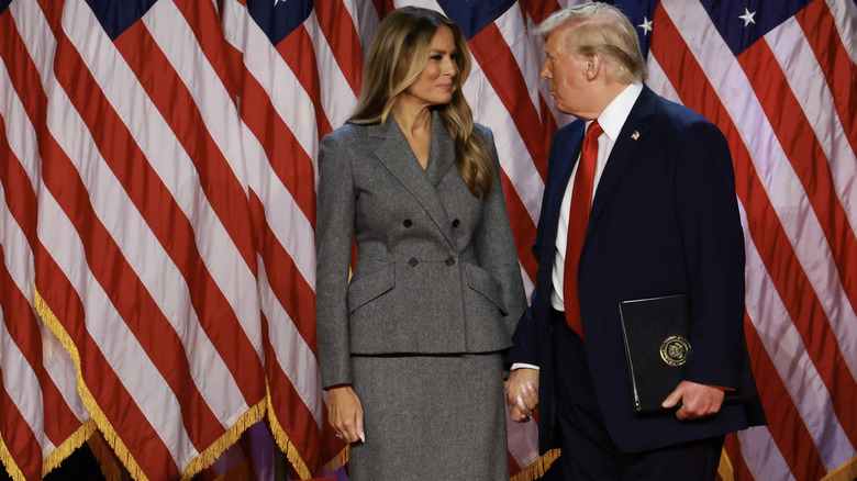 Melania and Donald Trump standing in front of American flags