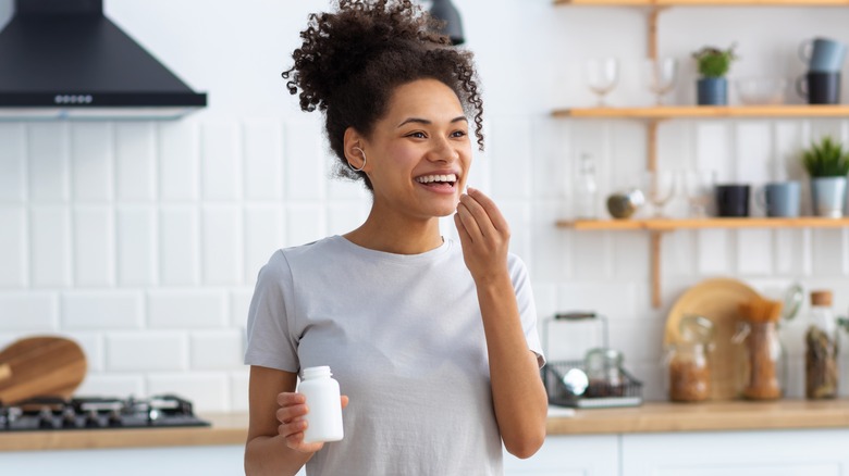 woman standing in a kitchen taking supplements 