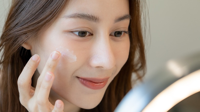 Asian woman applying cream on her face