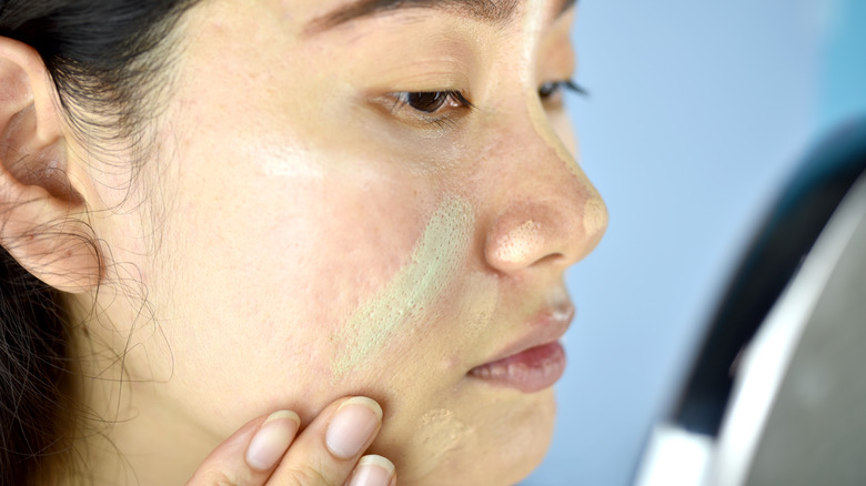 woman applying green concealer