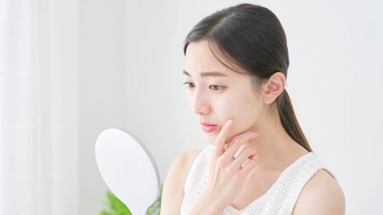 woman inspecting her face in the mirror