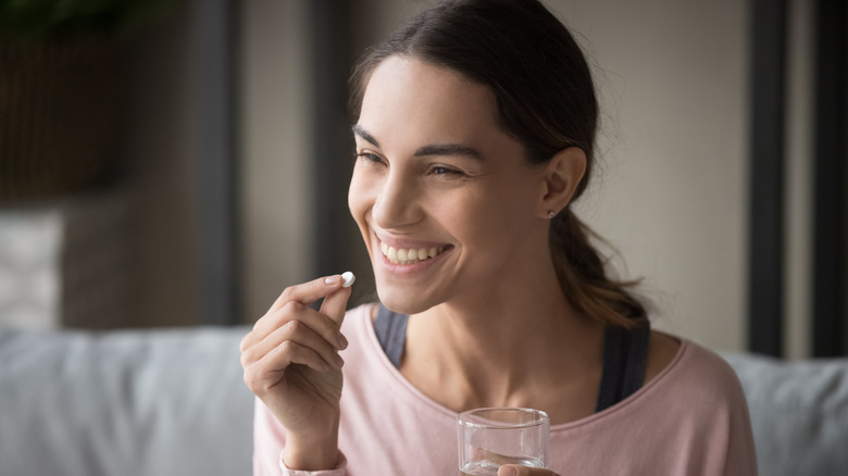 young woman holding pill and glass of water