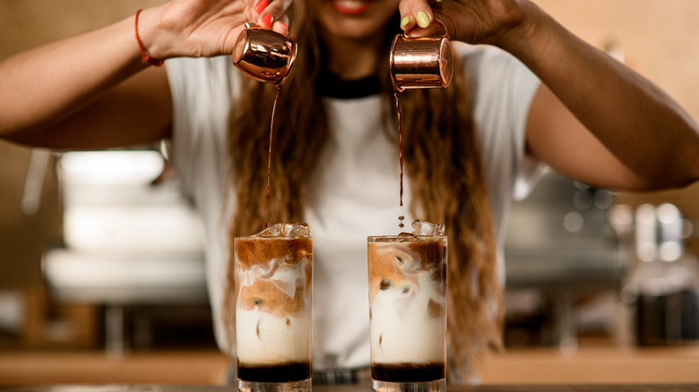 Barista pours espresso shots into two iced lattes