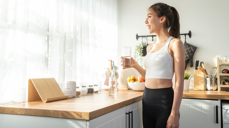 Woman stands in kitchen drinking water