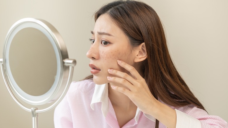 Woman examines her acne in mirror