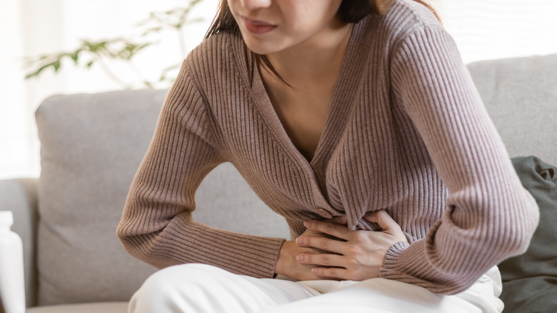 Woman suffers from stomach cramps while sitting on sofa