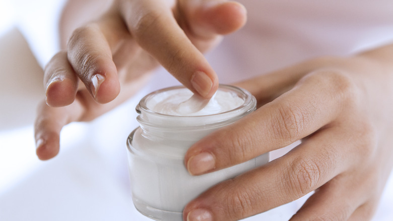 finger dipping into cosmetic jar