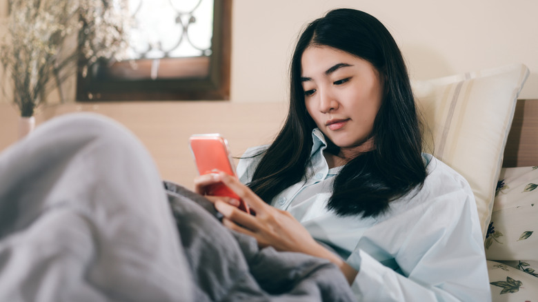 woman scrolling phone in bed