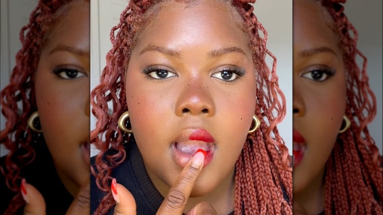 woman applying red lipstick with fingertip