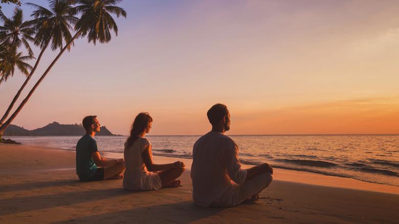 People meditating on beach at sunset