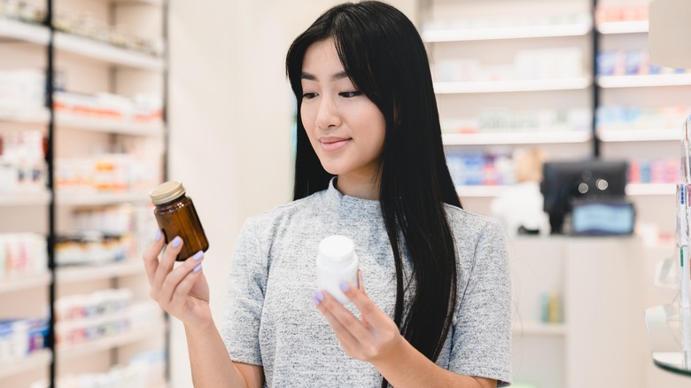 asian woman comparing bottles in pharmacy aisle