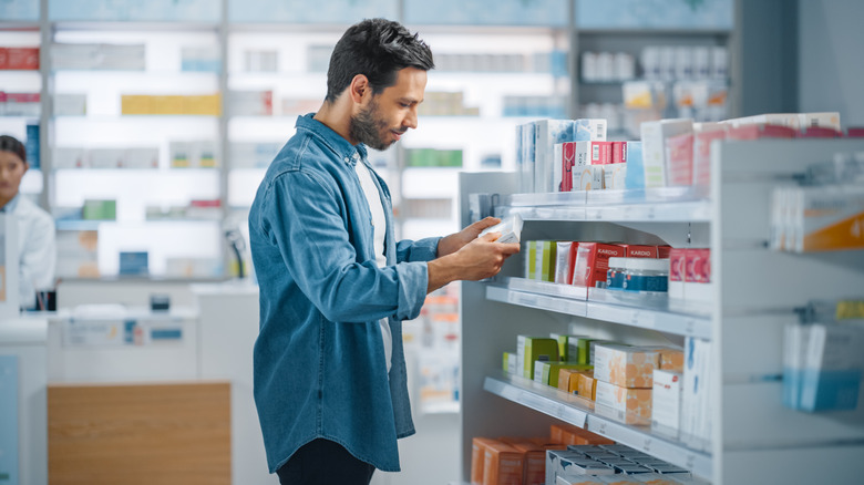 man looking at medicine vitamins in pharmacy aisle