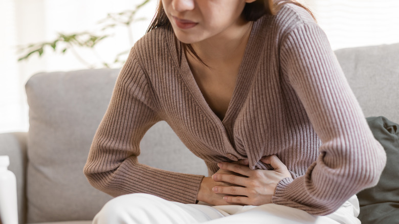 woman holding stomach in pain sitting on couch