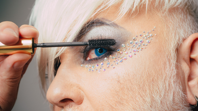 White-haired man applying mascara