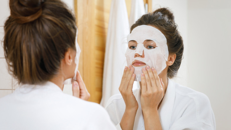 Woman adjusting sheet mask in mirror