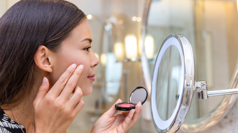 Woman applying cream blush on cheek