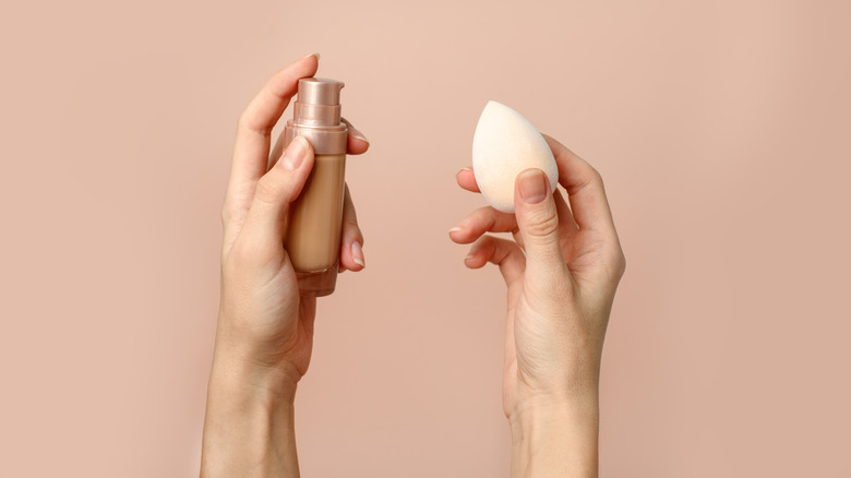 Hands holding foundation and makeup sponge