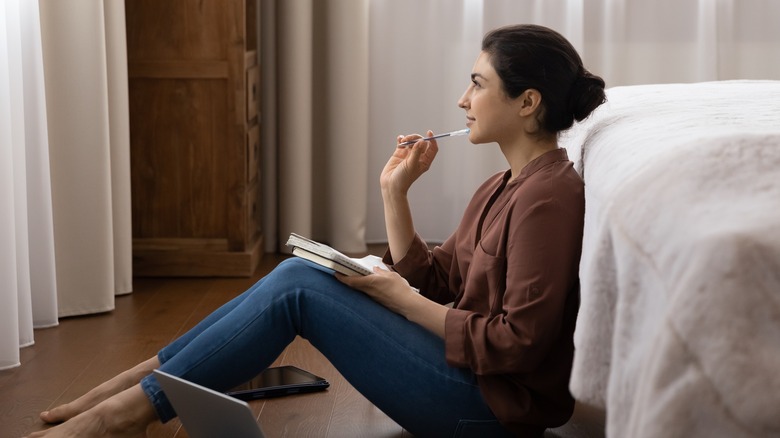 Woman contemplates while holding pen and notebook