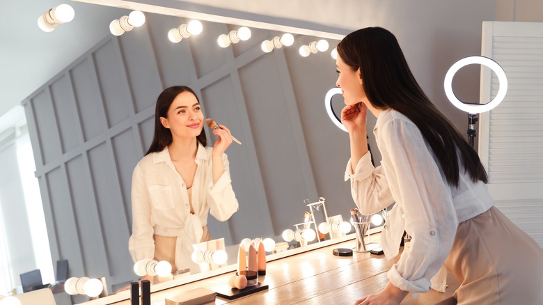 woman applying makeup in lighted mirror