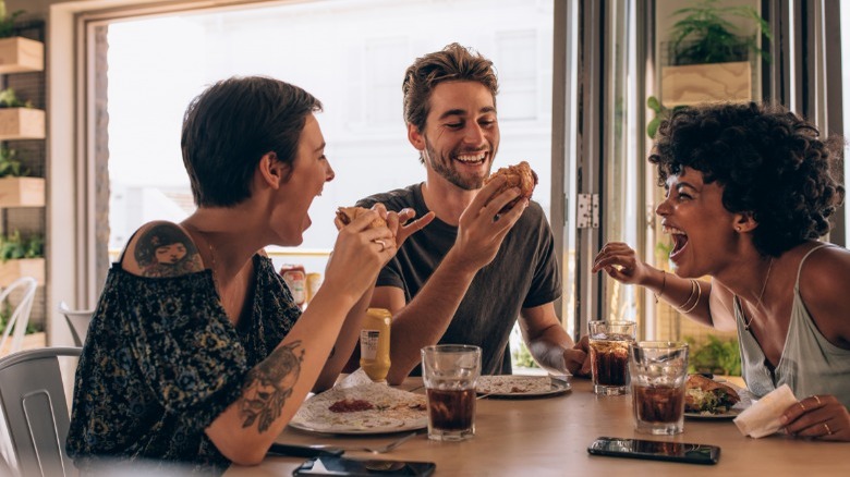 Three people laughing and eating at table