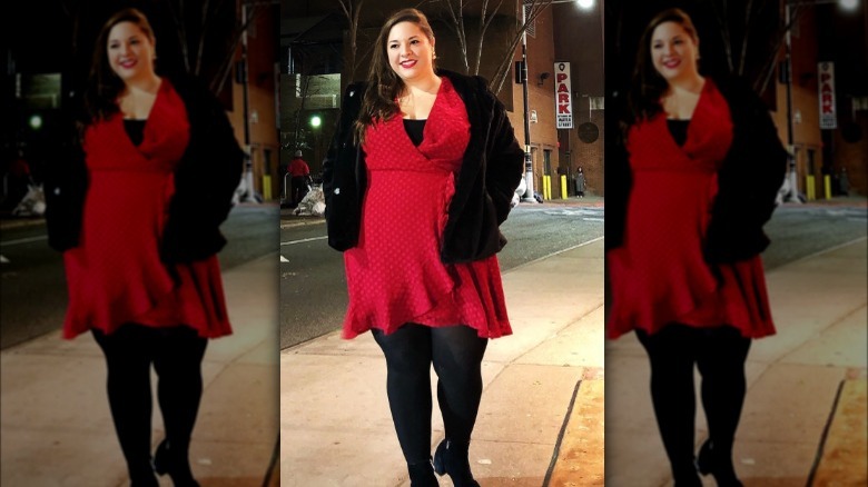 Woman on sidewalk in red dress and black coat