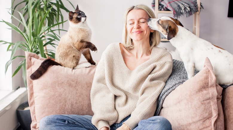 Woman on couch with dog and cat, smiling