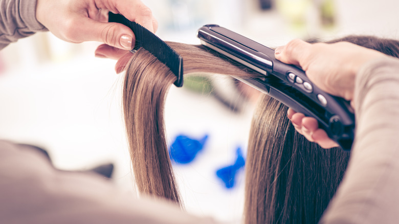 Close up of hairdresser using straightening iron 