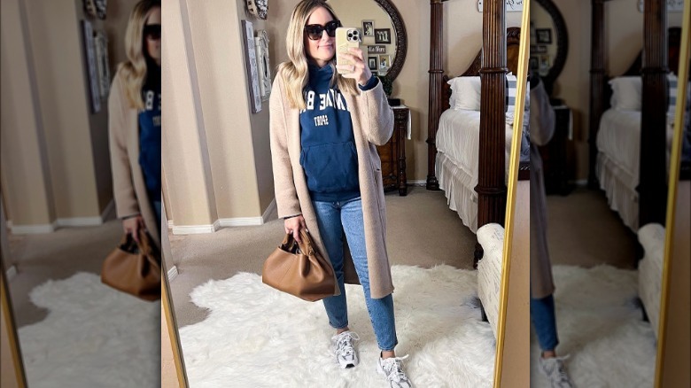 Woman takes selfie wearing tan coatigan, jeans, and hoodie 