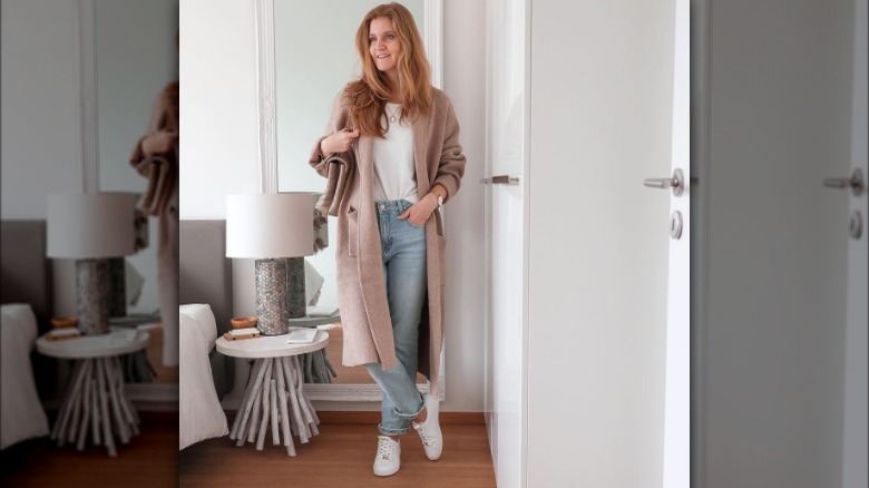 Woman poses in light wash jeans, white tee, and tan coatigan 