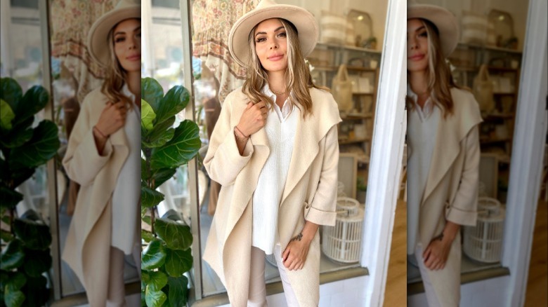 Woman poses in white jeans and button up with cream hat and coatigan 