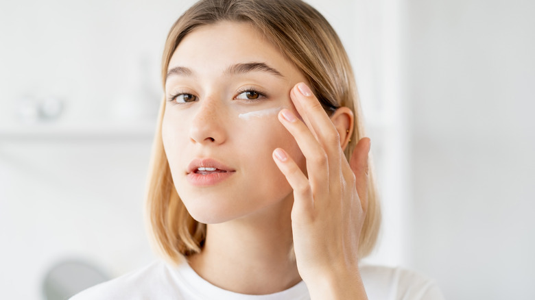 Woman applying skincare product under eyes