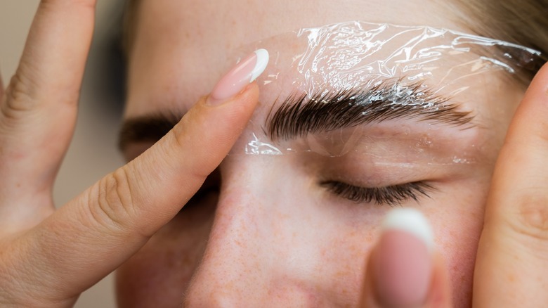 A woman using plastic wrap on eyebrows