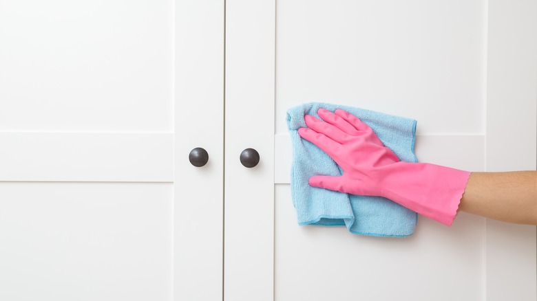 pink gloved hand cleans closet doors with blue microfiber towel 